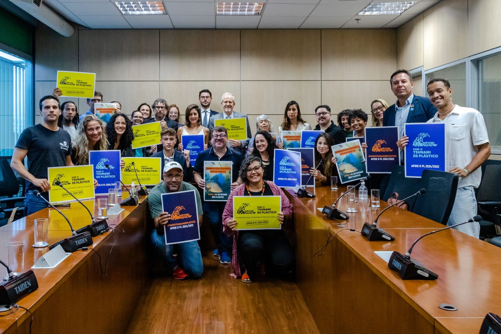 Integrantes da coalizão com cartazes Apoie o PL 2524/2022 em sala de reunião