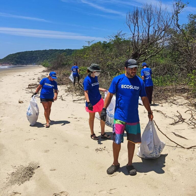 Voluntários com camisetas do Ecosurf recolhem lixo na areia durante limpeza de praia