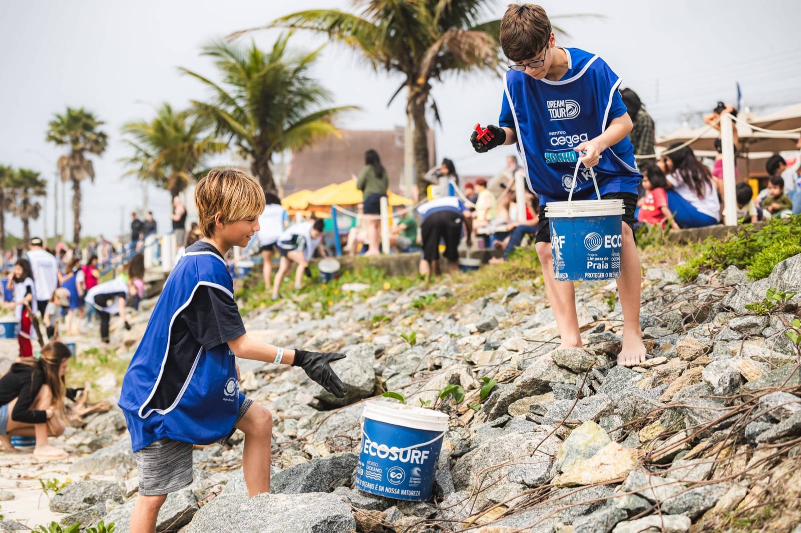 Jovens voluntários recolhem resíduos entre as pedras com baldes do Ecosurf