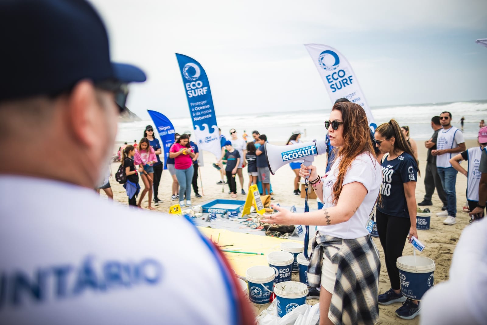 Facilitadora do Ecosurf fala ao megafone para os voluntários na praia