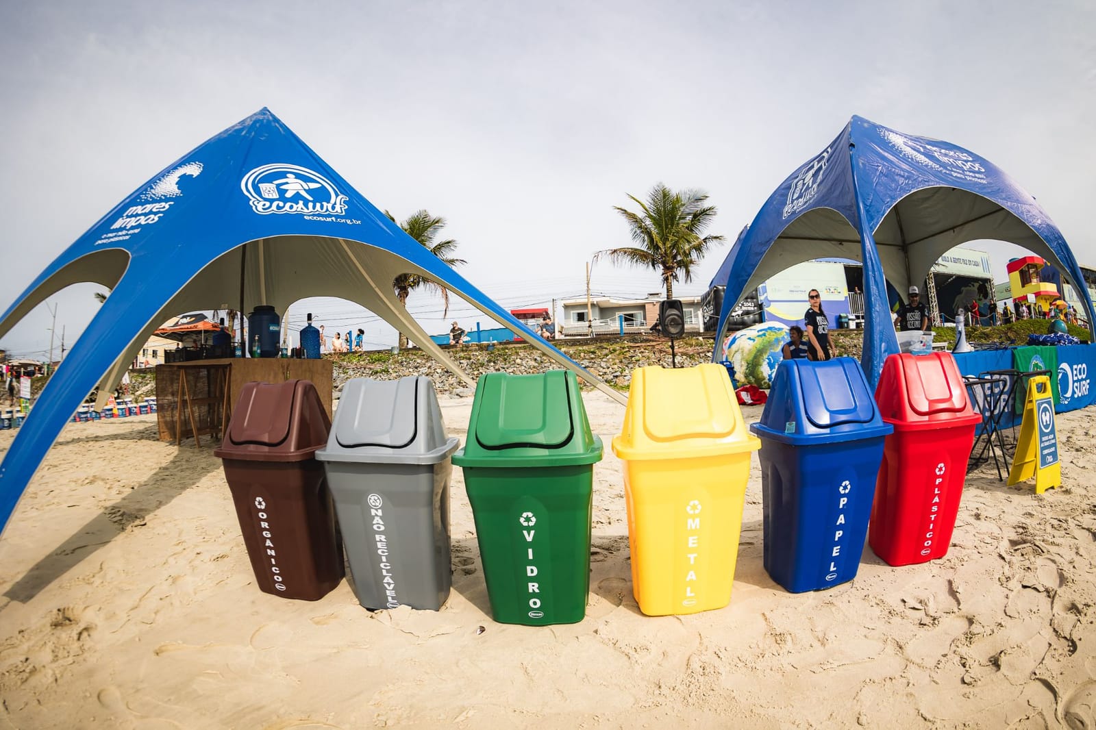 Lixeiras de coleta seletiva nas cores de cada material entre as tendas do Ecosurf