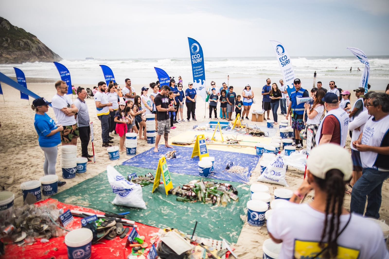 Voluntários em roda ao redor das lonas do Raio-X do Lixo, diante do mar