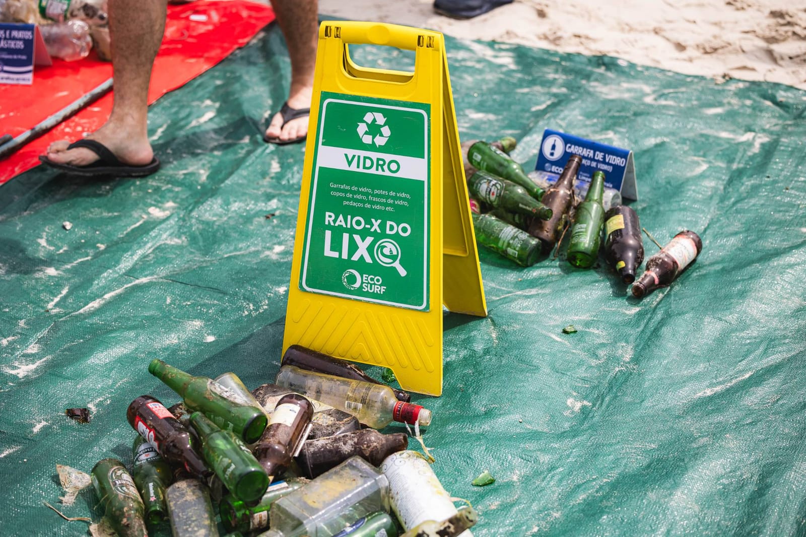 Garrafas de vidro recolhidas na praia ao lado da placa Vidro do Raio-X do Lixo