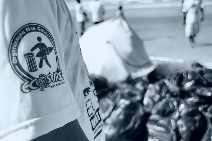 Voluntário com camiseta Ecosurf ao lado de sacos de resíduos coletados