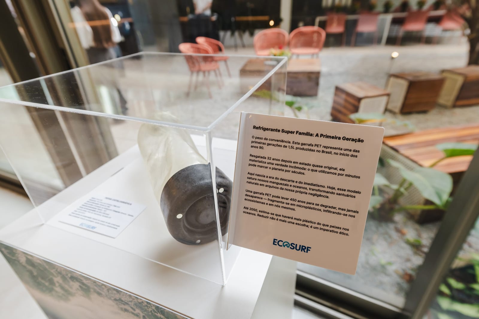 Garrafa PET de primeira geração exposta em cúpula de acrílico com texto curatorial