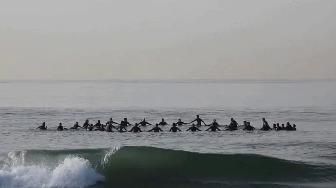 Surfistas de mãos dadas formando uma roda no mar