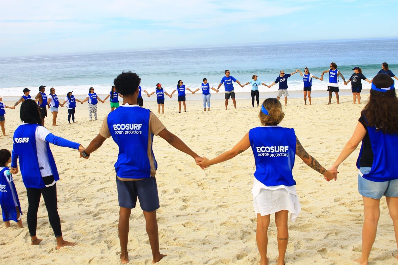 Voluntários do Ecosurf de mãos dadas formando uma roda na praia