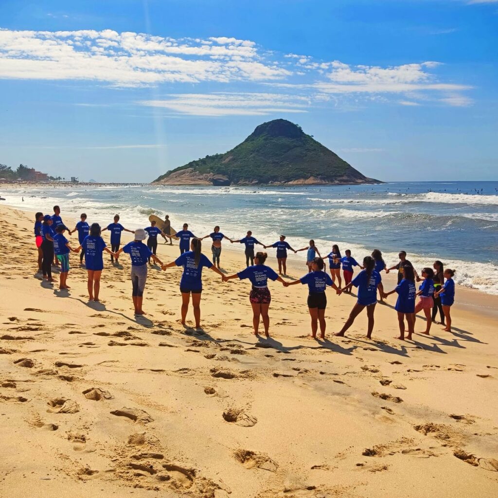 Voluntários com camisetas Nosso Oceano de mãos dadas em roda na areia da praia