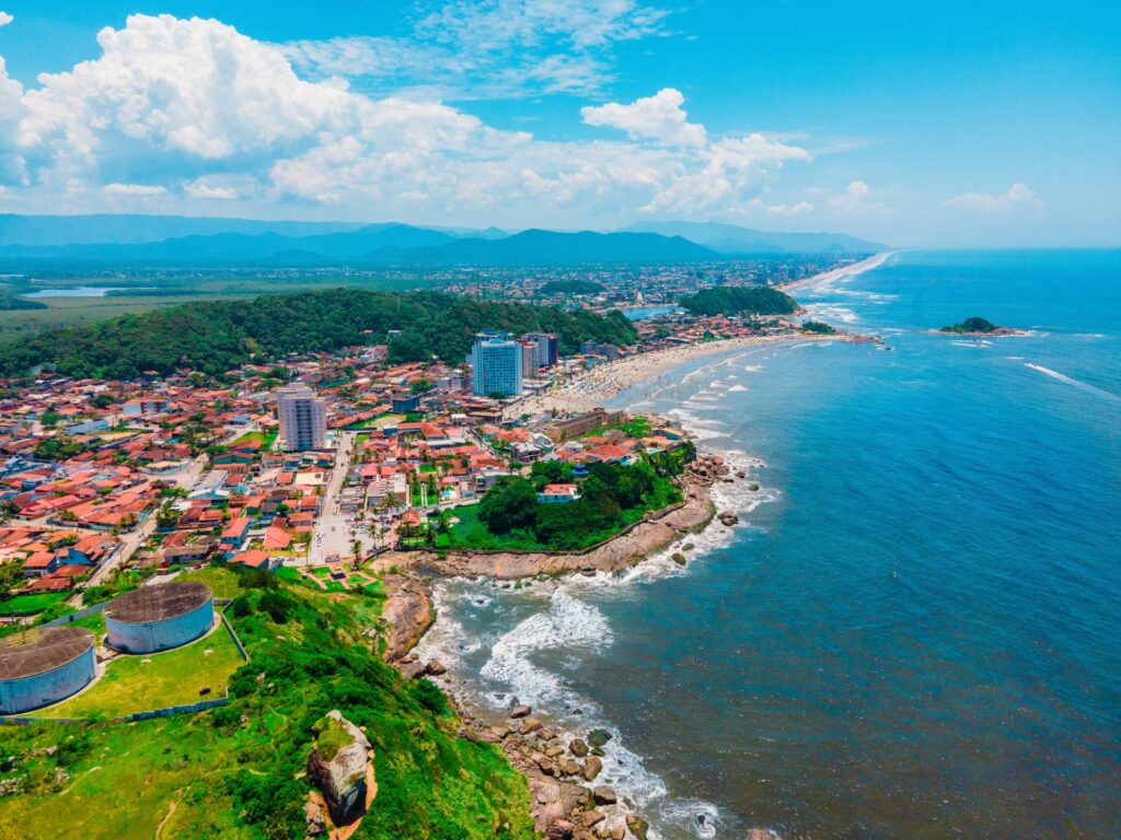 Vista aérea do litoral de Itanhaém, com costão rochoso, praia, casas e a serra ao fundo