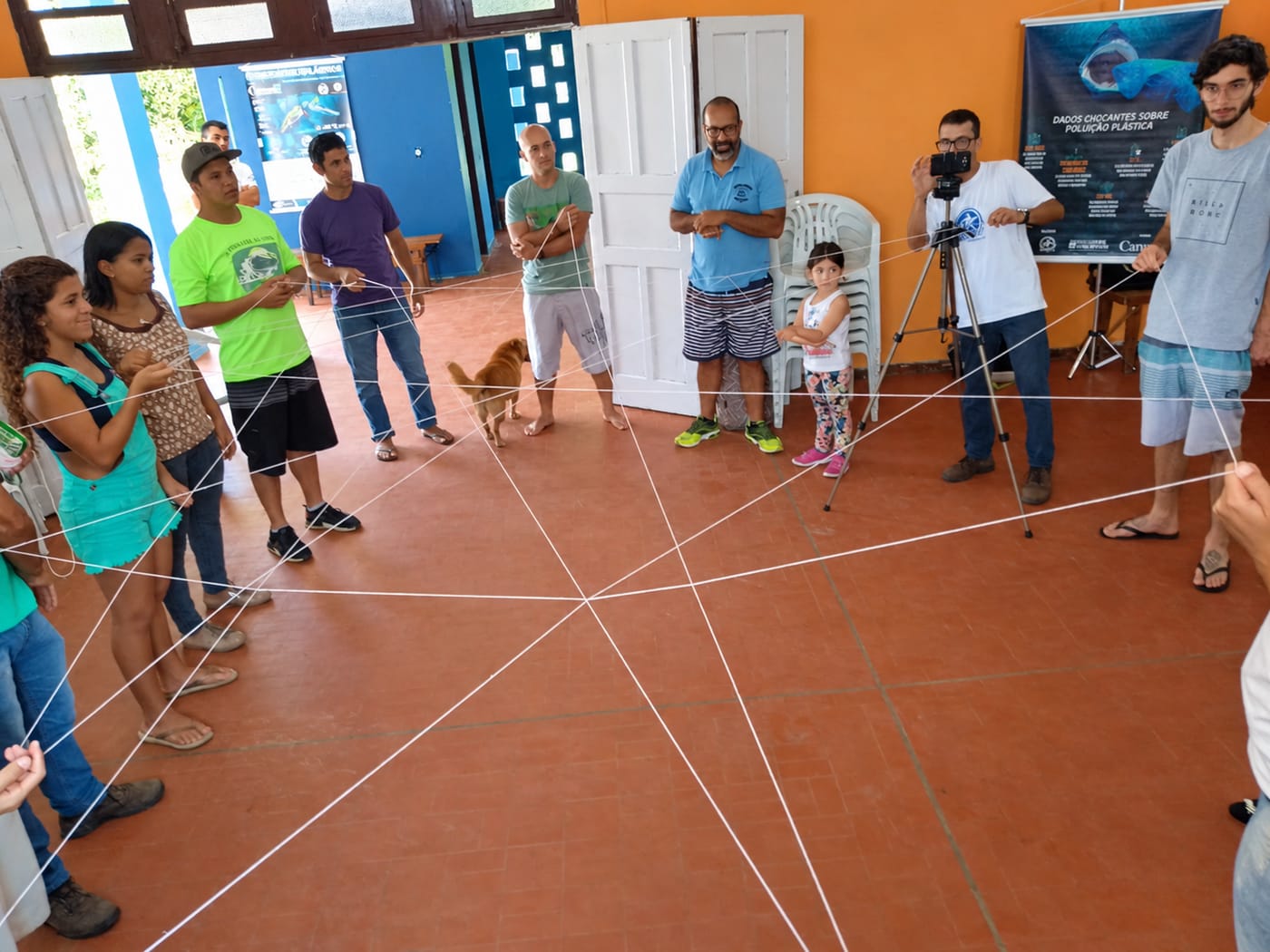 Participantes em roda, ligados por fios que formam uma teia no chão, durante oficina do Ecosurf